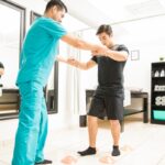 Physiotherapist Helping Athlete To Walk Between Cones In Hospital Physiotherapist Helping Athlete To Walk Between Cones In Hospital