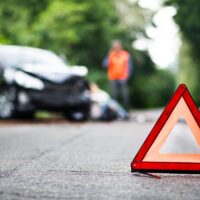 A close up of a red emergency triangle on the road in front of a car after an accident.