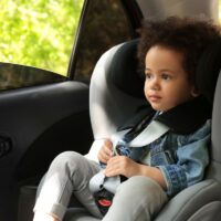 Cute African-American child sitting in safety seat inside car. Danger prevention