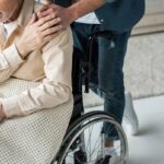 cropped view of caring son holding hands with disabled senior father in wheelchair at home