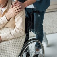 cropped view of caring son holding hands with disabled senior father in wheelchair at home