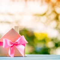 Home model tied with pink ribbon on bokeh in the public park, The buy new house or real estate as gift to family or the one loved concept.