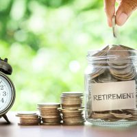 Hand putting Coins in glass jar with retro alarm clock for time to money saving for retirement concept